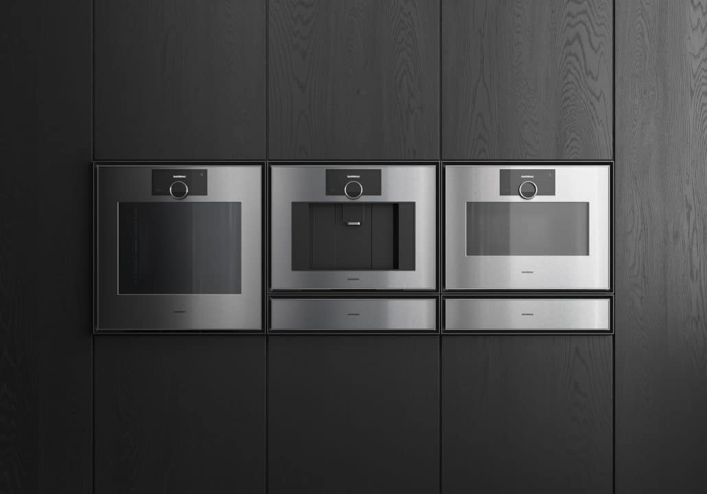 Drei silberen Geräte von Gaggenau, die nebeneinander eingebaut sind in dunklen Holzschränken.