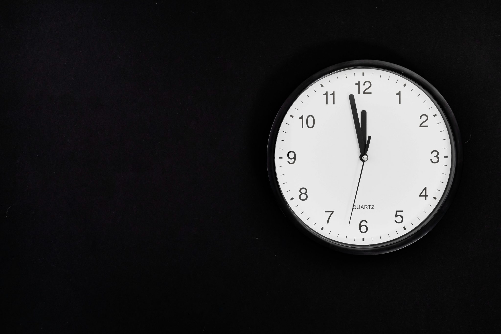 Eine weiße Wanduhr, die an einer schwarzen Wand hängt.